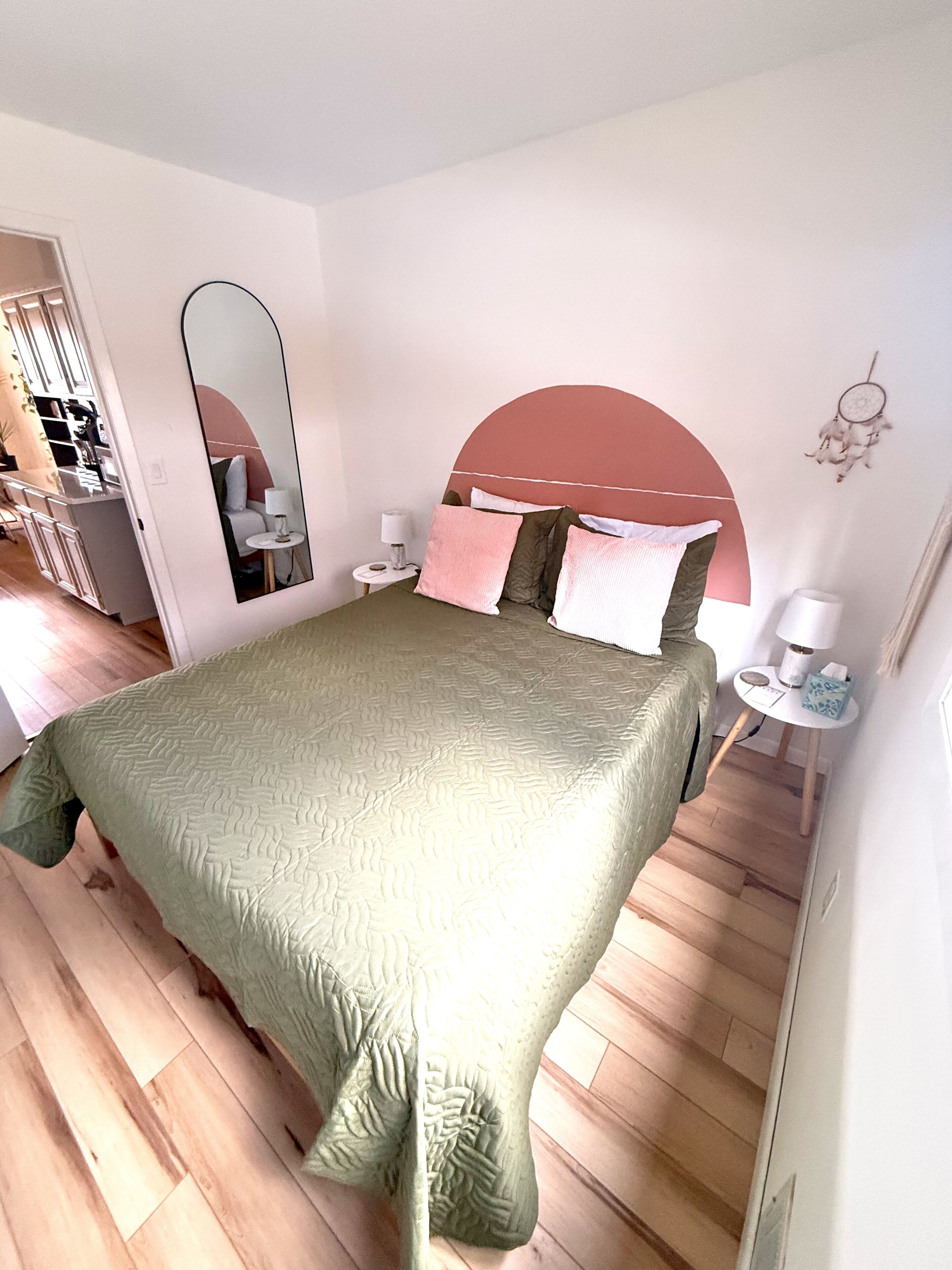 A bedroom with a bed, a nightstand, a mirror, and a dreamcatcher on the wall.