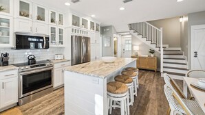 Een moderne keuken met witte kasten, roestvrijstalen apparatuur en een centraal eiland met krukken.