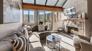 A modern living room with a sectional sofa, a round coffee table, a fireplace, and a TV mounted on the wall.