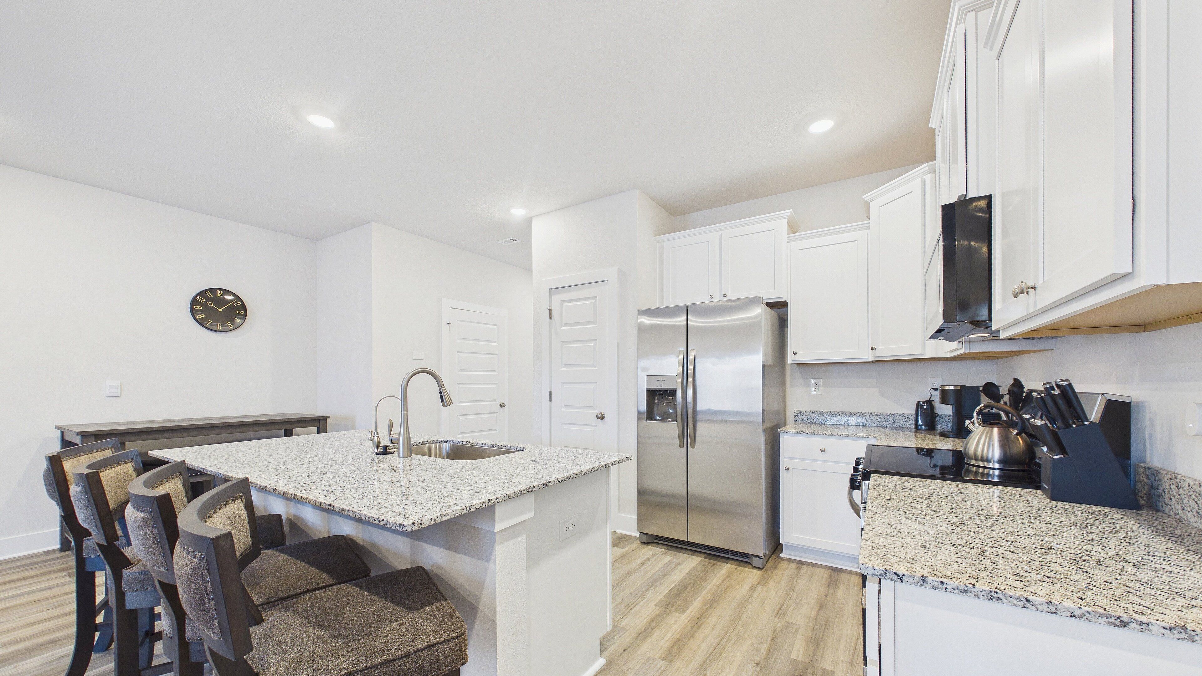 A modern kitchen with white cabinetry, a stainless steel refrigerator, granite countertops, and a built-in island with bar stools.