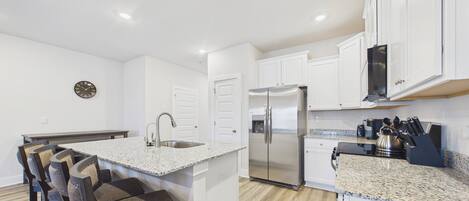 A modern kitchen with white cabinetry, a stainless steel refrigerator, granite countertops, and a built-in island with bar stools.