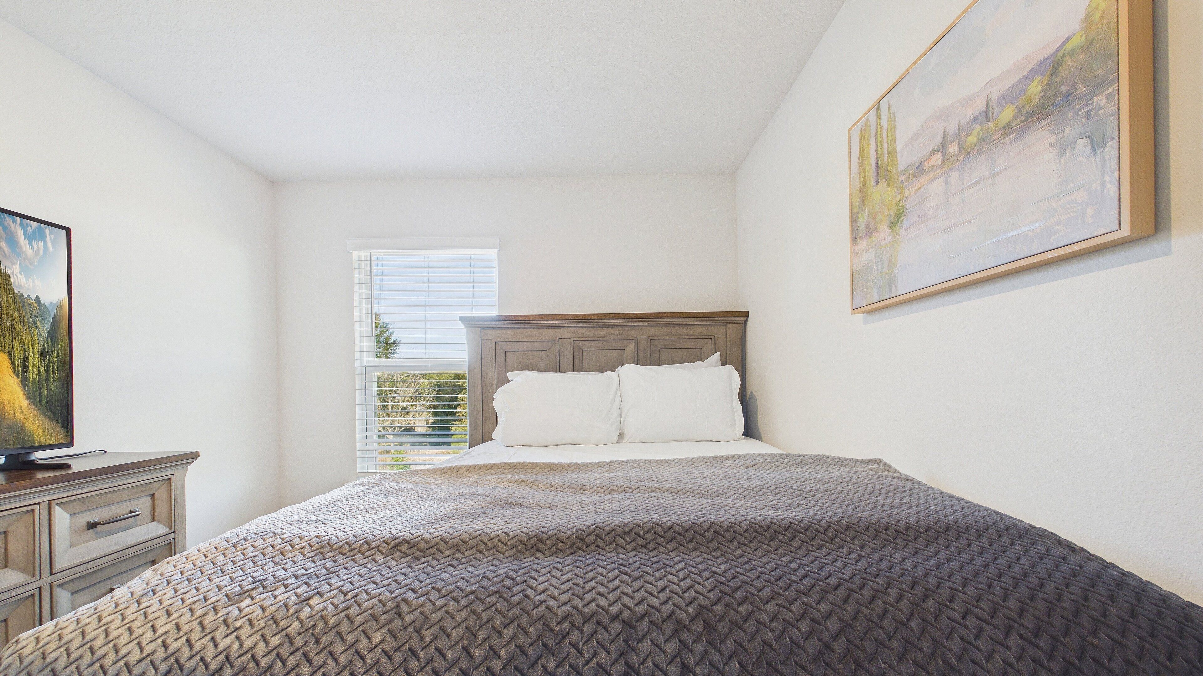 Un dormitorio con cama, cómoda, un cuadro y ventana con persianas.