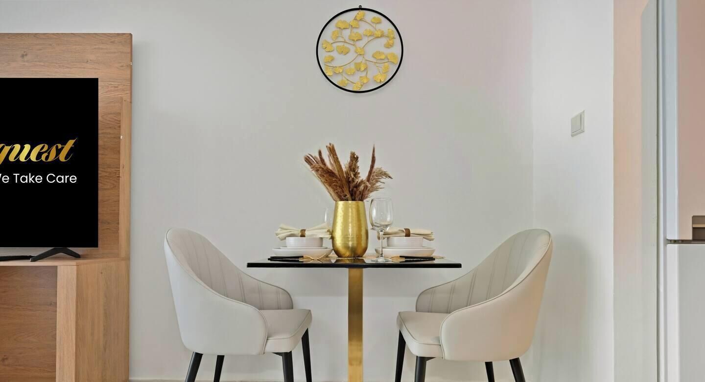 A dining area with a blackboard, two white chairs, a gold vase, and a small table.