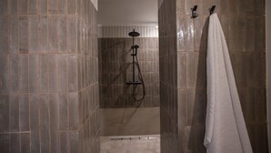 Zona de bany amb parets revestides de rajoles, plat de dutxa i tovallola blanca penjada d'un ganxo.