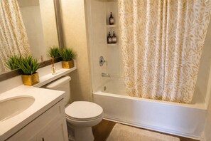 Ein Badezimmer mit Toilette, Waschbecken, Spiegel, Duschvorhang und zwei Blumentöpfen.