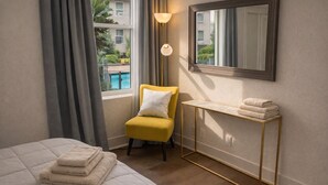 Hotellihuone, jossa on sänky, tuoli, pyyhkeillä varustettu pöytä, ikkuna verhoilla ja seinälle kiinnitetty peili.
