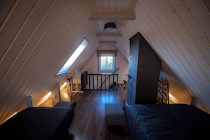 Een gezellig zolderkamer met houten latten, twee bedden, een klein tafeltje en een raam dat natuurlijk licht biedt.