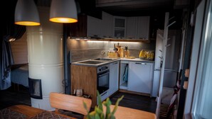 Una cucina compatta con piano cottura, lavello e pensili bianchi. Si nota una panca in legno e un tavolo con tovaglia fantasia.