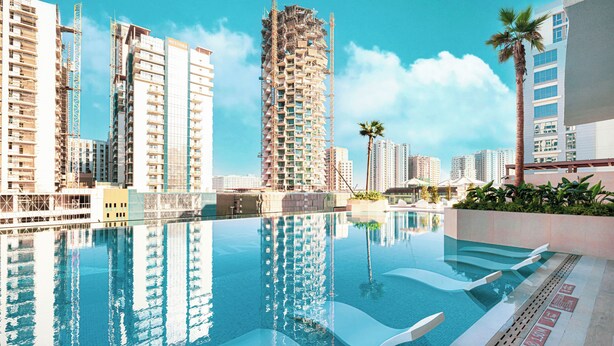A swimming pool with modern loungers, surrounded by high-rise buildings and palm trees. - Binghatti Phantom Suites by Hostiva (Dubai)