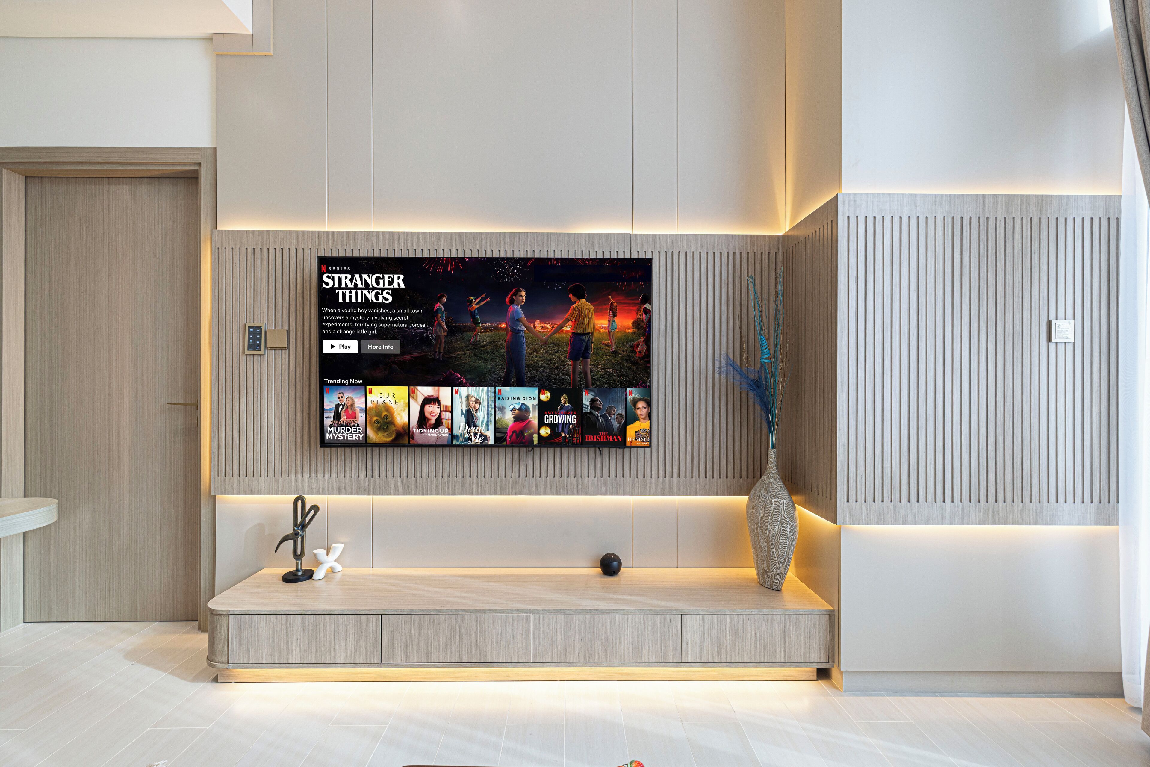 Ein modernes Wohnzimmer mit großem Flachbildfernseher an der Wand, einer eingebauten Sitzbank mit Vase und einem minimalistischen Design.