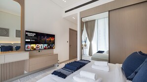 A modern hotel room with a large bed, a flat-screen TV mounted on the wall, a walk-in closet, and a large window with curtains. - Binghatti Phantom Suites by Hostiva (Dubai)