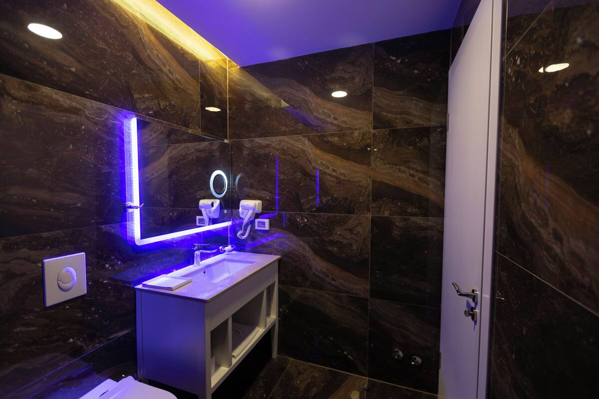 A modern bathroom with marble walls, a white sink, and a mirror with blue LED lighting.