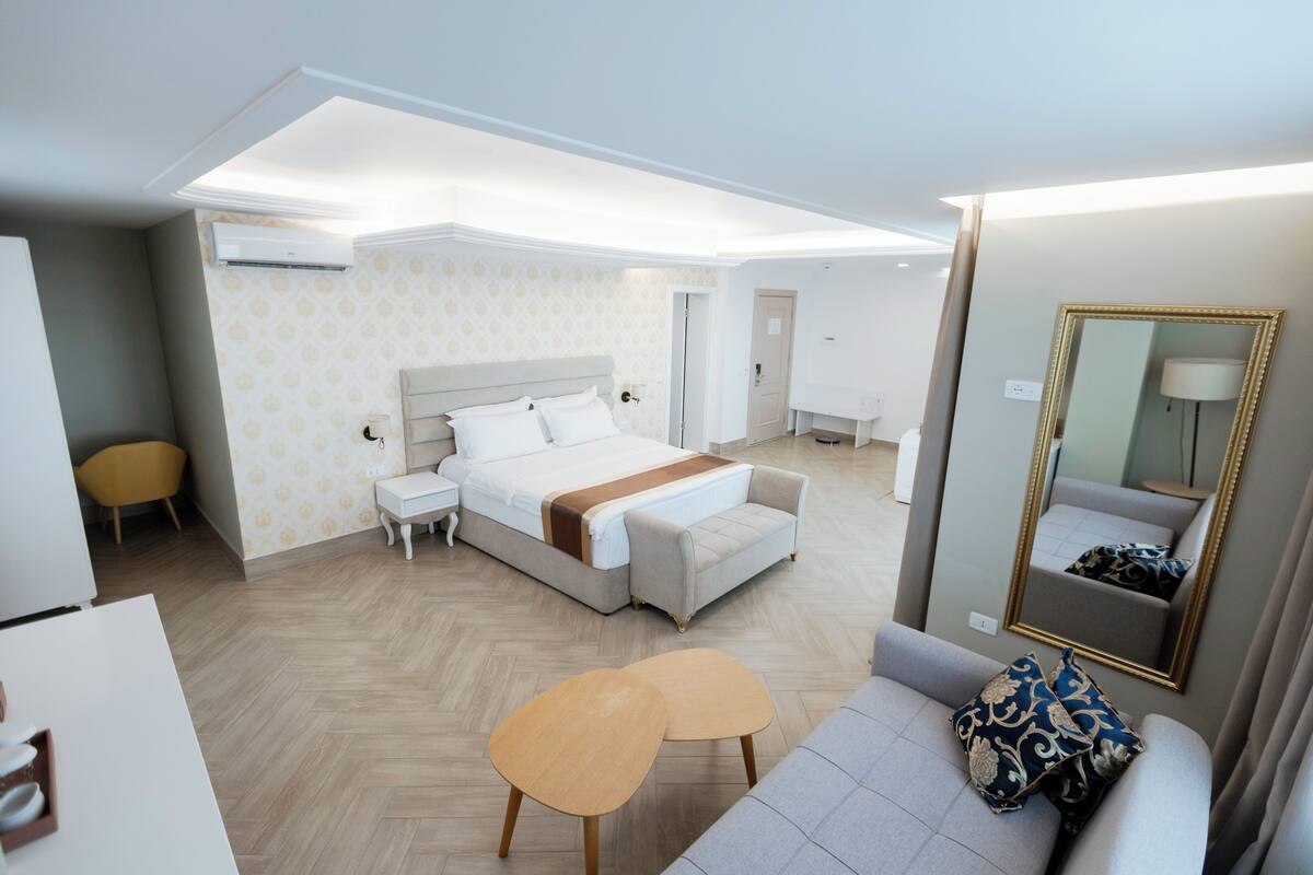 A modern hotel room with a large bed, a sofa, a small table, and a mirror.