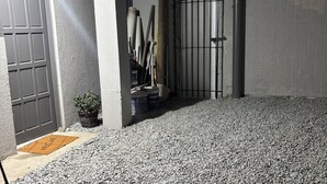 Un espacio exterior cubierto con suelo de grava, una reja metálica y una puerta con felpudo.