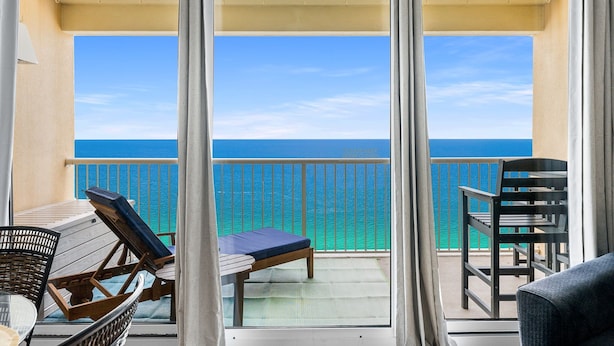 Un balcon avec vue sur l’océan, un lit et deux chaises.
