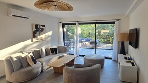 A modern living room with a sofa, ottoman, coffee table, and a TV on the wall. - CORSICA: LOUNICELI Villa with air conditioning, a pool, beaches, shops, and mountains (Zonza)