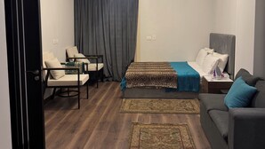 A modern hotel room with a bed, a sofa, a chair, a small table, and a decorative rug. - Peaceful Zayed Rooftop Stay Near Arkan & Park St. (Al Sheikh Zayed City)