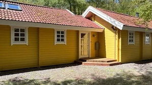 Un edificio amarillo con techo de tejas rojas, una puerta principal y un pequeño porche.
