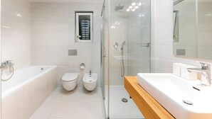 Un baño moderno con ducha envuelta en vidrio, tocador de madera, inodoro y bidés.