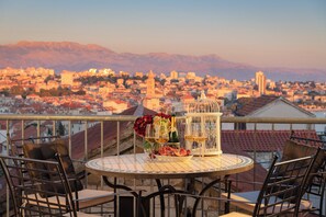 A balcony with a table set for two, featuring a bottle of wine, glasses, and a flower arrangement. The balcony overlooks a cityscape with mountains in the background. - A private oasis just 5 minutes from Diocletian's Palace (Split)