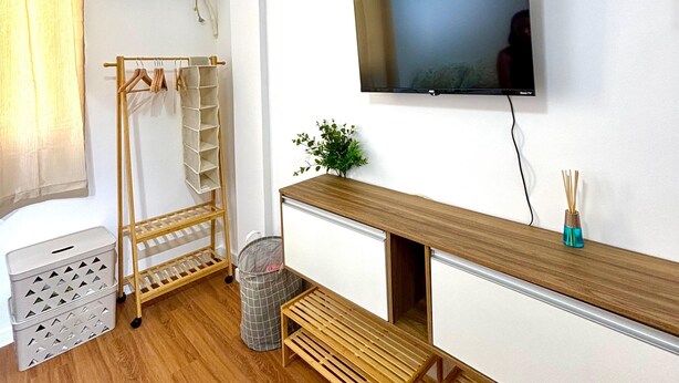 Une chambre moderne avec un plancher en bois, un téléviseur fixé au mur, un banc en bois, un porte-vêtements et une petite plante.