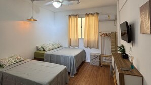 Une chambre avec deux lits, un ventilateur de plafond, une télévision et un banc en bois.