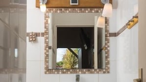 Un baño con un lavamanos blanco, un espejo con un marco de mosaico y una toalla colgada en un perchero.