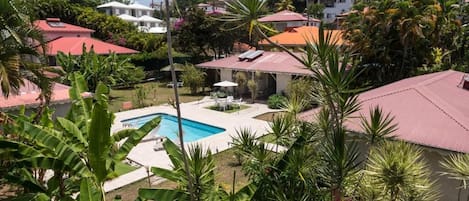 Ett bostadsområde med en swimmingpool omgiven av frodig grönska och hus med röda tak.