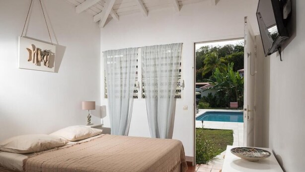 Un dormitorio con cama, mesita de noche, lámpara, televisor montado en la pared y vista a una piscina exterior.