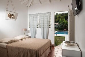 Un dormitorio con cama, mesita de noche, lámpara, televisor montado en la pared y vista a una piscina exterior.