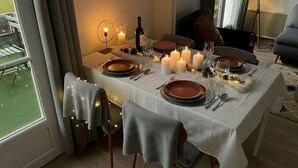 Ein Esstisch, gedeckt für vier Personen, mit Kerzen, Wein und einer Flasche.