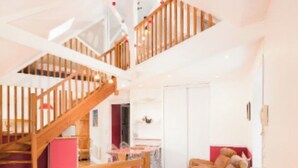 Een ruime woonkamer met een houten trap, een rode bank en een eettafel.
