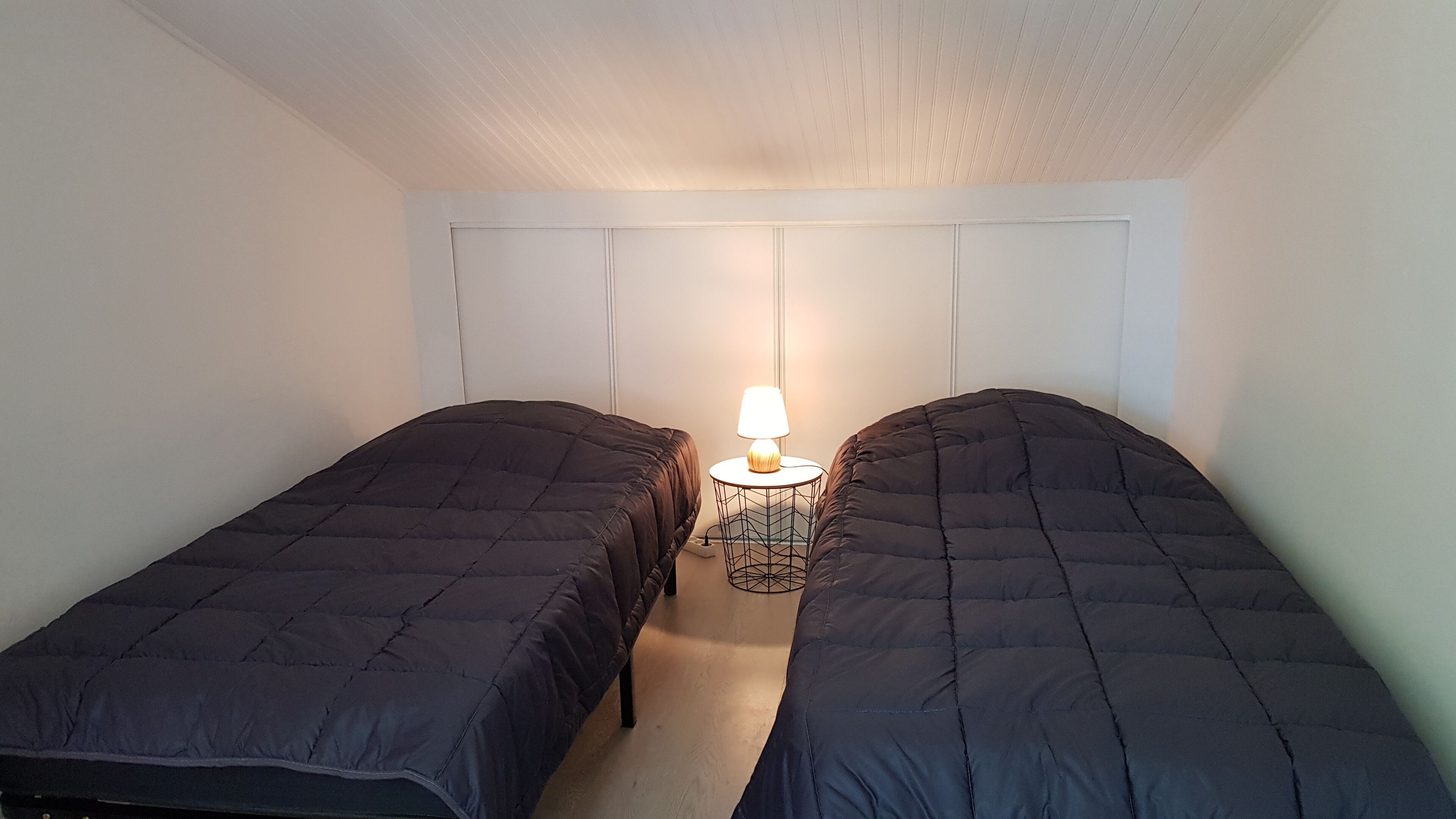 Ein kleines Schlafzimmer mit einem Einzelbett, zwei Einzelbetten, einem Nachttisch mit Lampe und einer weißen Decke.