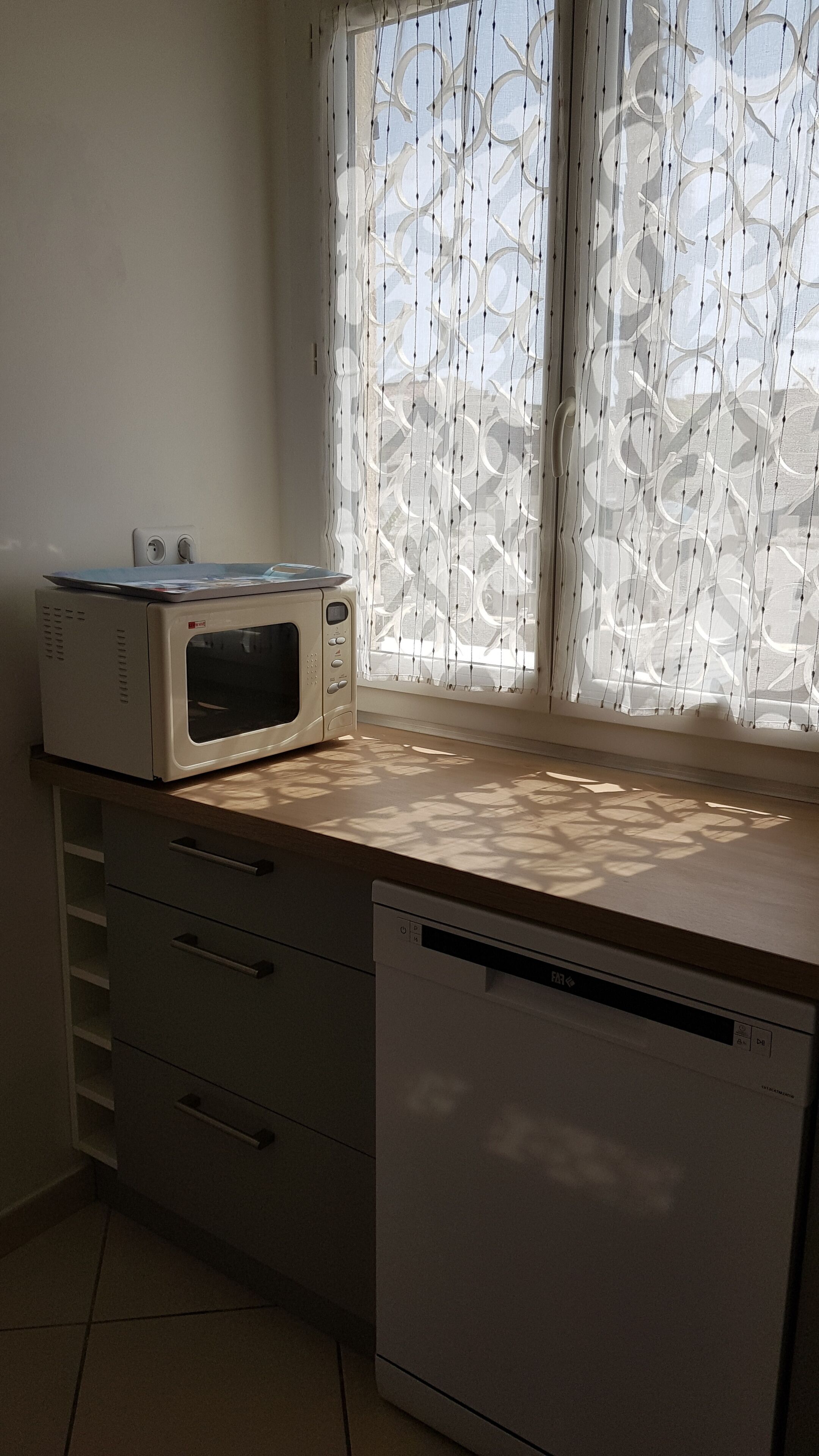 Una cocina equipada con microondas, lavavajillas y un ventanal con cortinas estampadas.