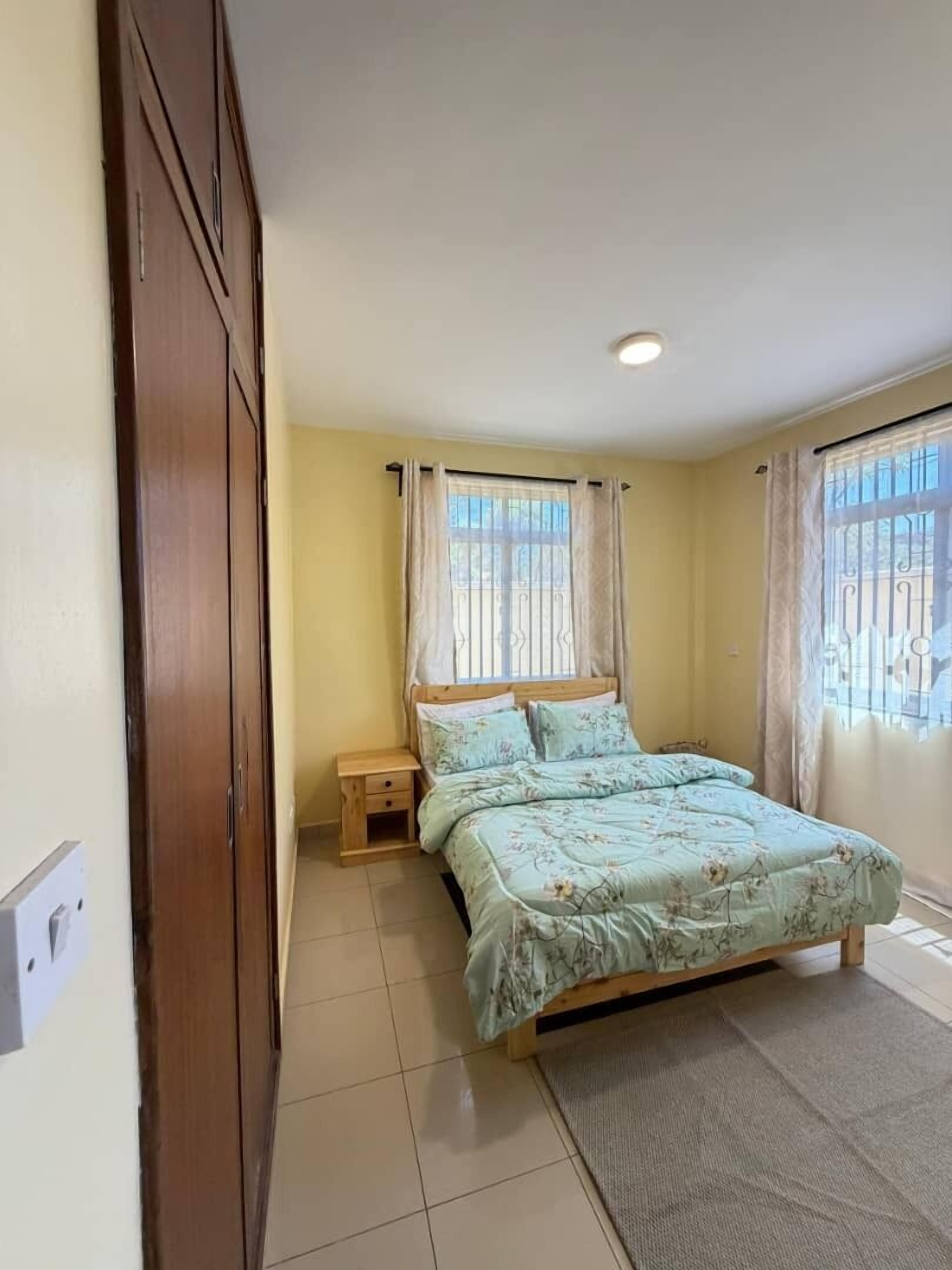 Un dormitorio con cama, mesitas de noche, un armario de madera y una ventana con cortinas.