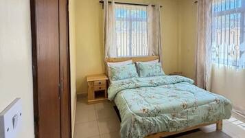 Un dormitorio con cama, mesitas de noche, un armario de madera y una ventana con cortinas.