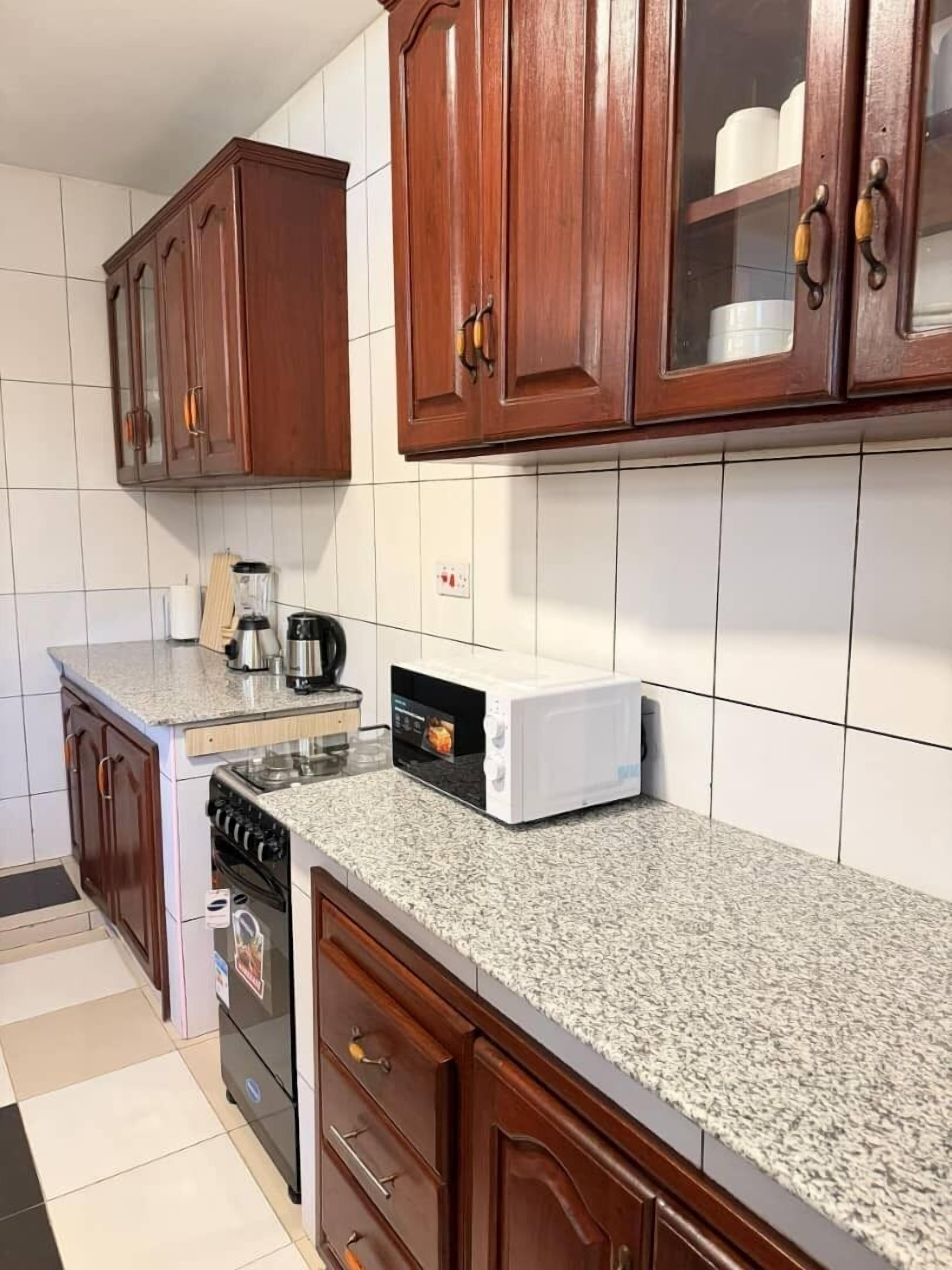 A kitchen with wooden cabinets, a granite countertop, a stove, a microwave, and a coffee maker.