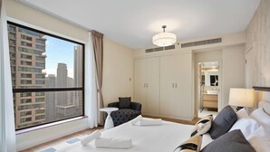 Et hotelværelse med en stor seng, et lille rundt bord, en stol, et garderobeskab og et badeværelse, der kan anes gennem en åben dør.