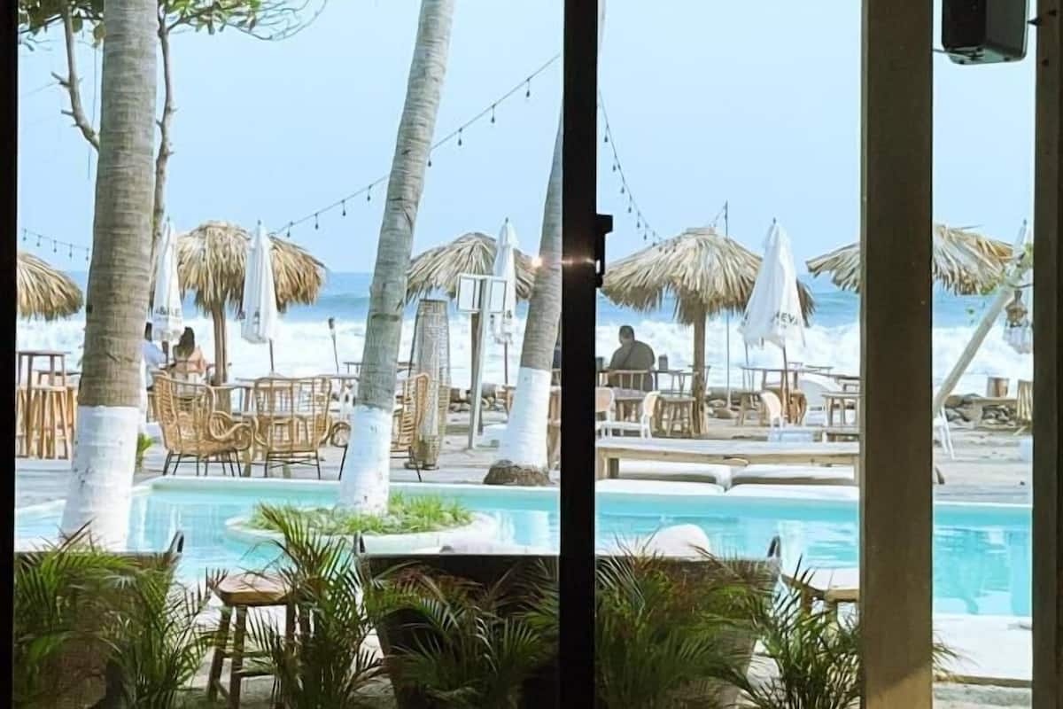 Zona de piscina con sillones reclinables, sombrillas y vista al océano.