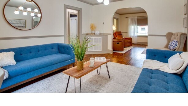 Een woonkamer met twee blauwe banken, een ronde spiegel, een houten salontafel en een hanglamp.