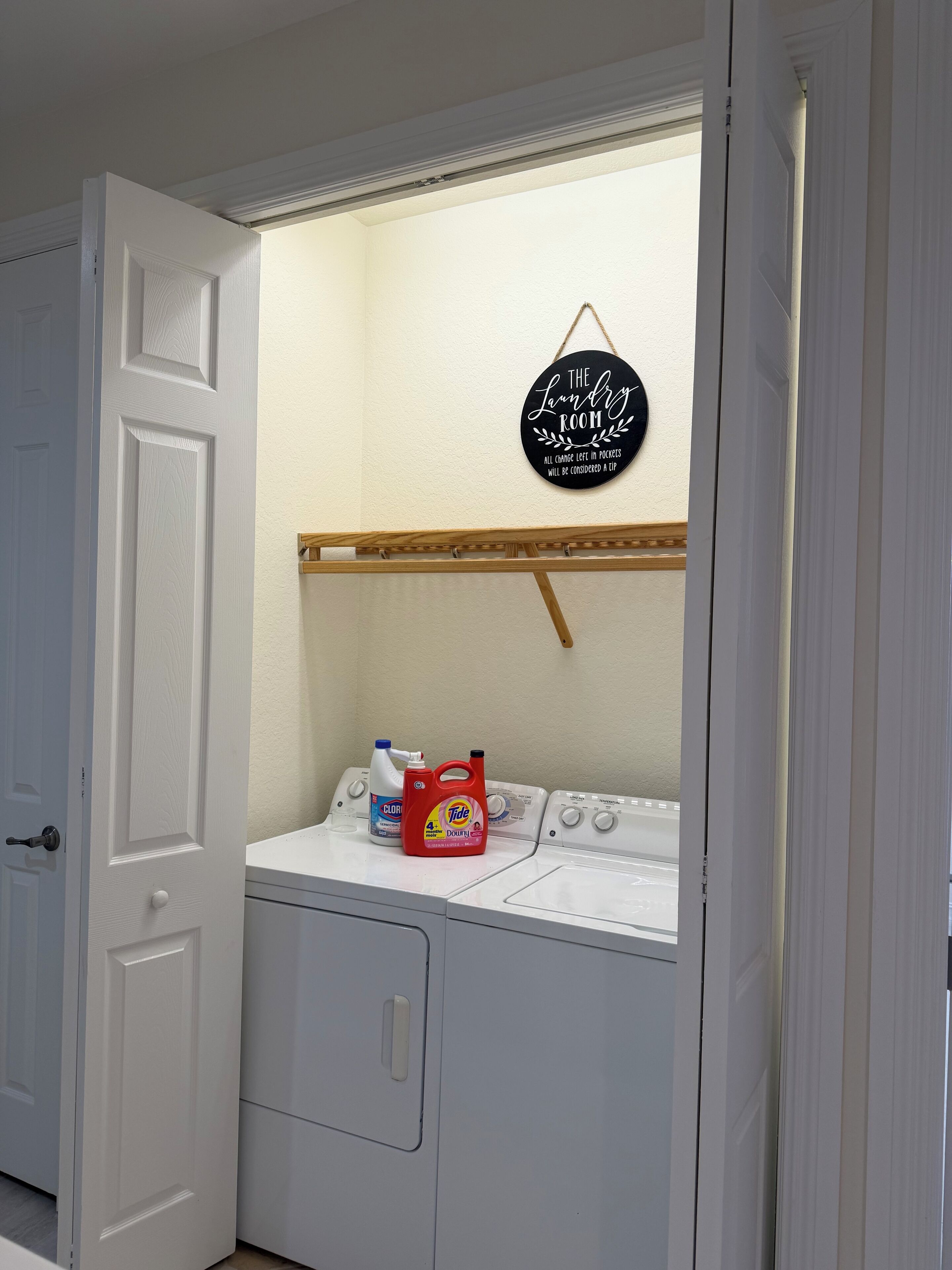 A laundry room with a hanging sign, a shelf, and a washing machine.