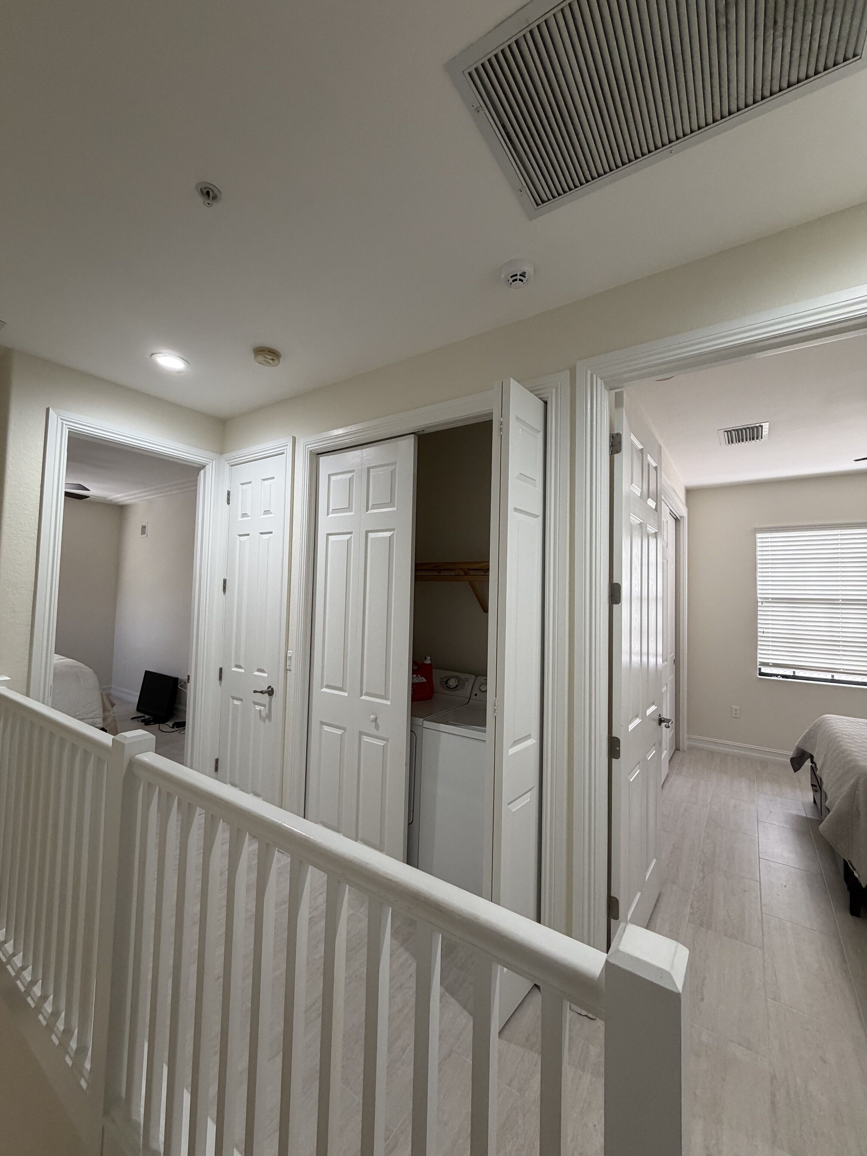A hallway with white doors leading to a laundry area, a radiator, and a window with blinds.