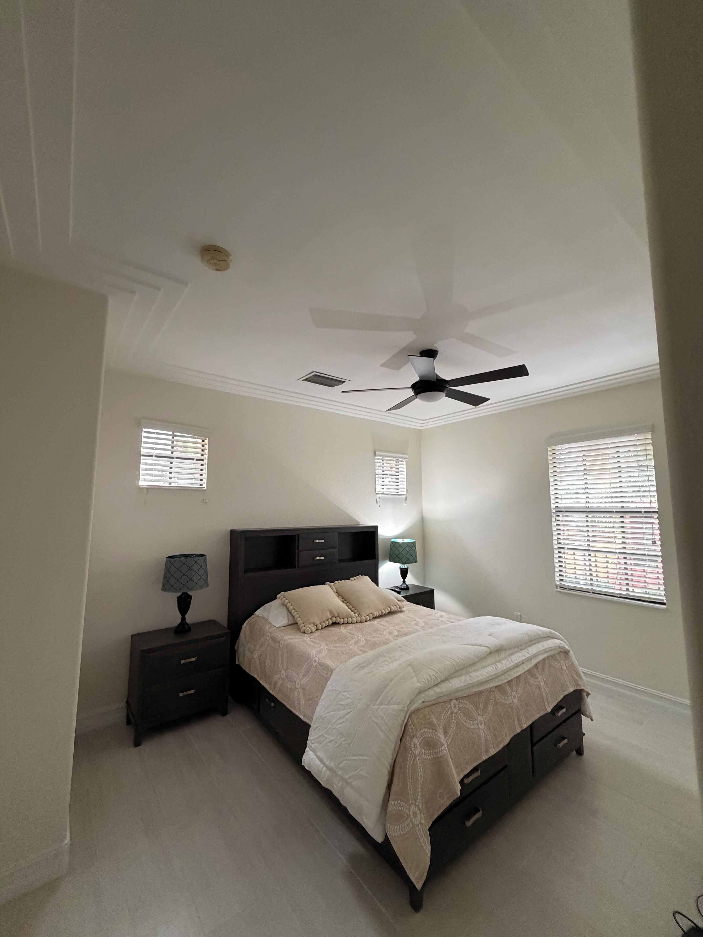 A bedroom with a bed, nightstands, a ceiling fan, and windows with blinds.