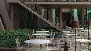A modern outdoor dining area with round tables and chairs, a staircase, and a balcony with seating. - Relax, Wander, Repeat—Lisbon’s Magical Light Show & History at Your Feet (Lisboa)