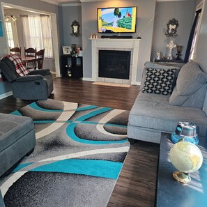 A living room with a fireplace, a television mounted above it, and a dining area with a table and chairs.