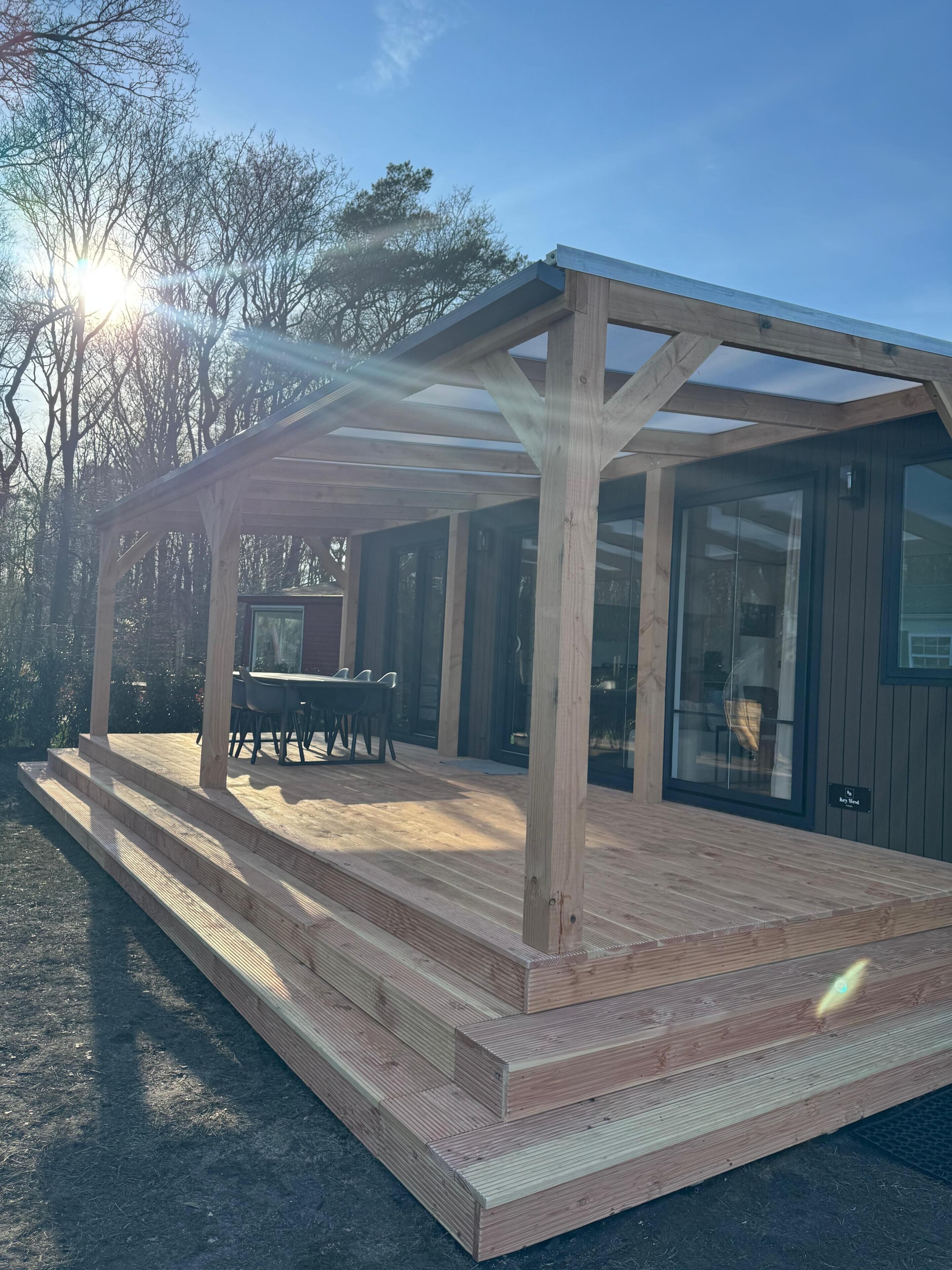 Eine Holzterrasse mit einer Pergola, einem Tisch und Stühlen sowie einer Glastür.