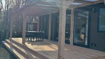 Eine Holzterrasse mit einer Pergola, einem Tisch und Stühlen sowie einer Glastür.