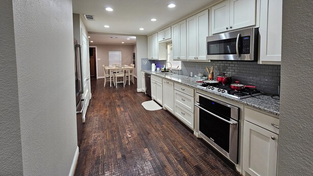 A modern kitchen with white cabinets, a stainless steel microwave, and a granite countertop. - 3-bedroom house in peaceful McKinney with cool AC for relaxing stays (McKinney)