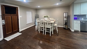 A dining area with a wooden floor, white chairs, a table with a vase of flowers, and a kitchen with white cabinets and a dishwasher. - 3-bedroom house in peaceful McKinney with cool AC for relaxing stays (McKinney)