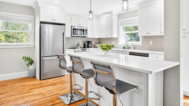 A modern kitchen with white cabinets, stainless steel appliances, and a central island with bar stools. - Charming Renovated Home, Cozy for All! Pet friendly! (New Windsor)